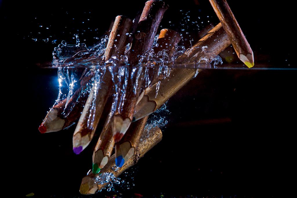 Lápices de colores atravesando la superficie del agua, fotografiados en el instante del impacto.
